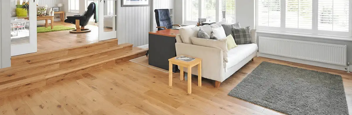 A modern living room with professionally installed laminate flooring, a beige sofa, a small side table, a gray rug, and large windows with white shutters in Wilmington, NC
